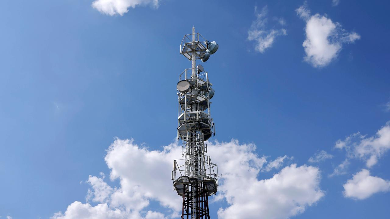 Der Sendemast ist vom Boden aus fotografiert. Darüber strahlt ein blauer Himmel mit wenigen Wolken.
