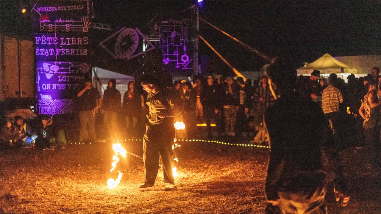 Menschen stehen um ein Feuer und feiern. Es ist Nacht.