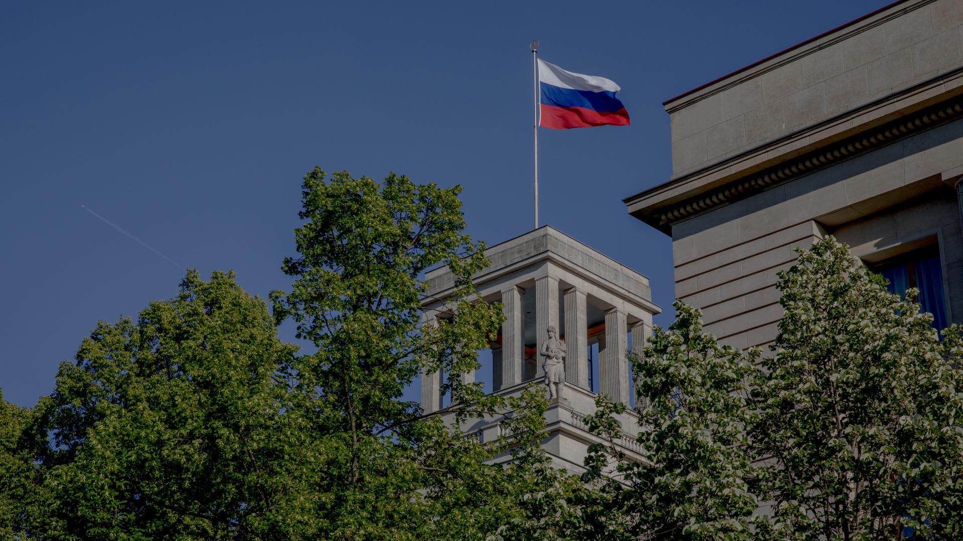 Die russische Fahne über der Botschaft der Russischen Föderation in Berlin und grüne Baumkronen. 