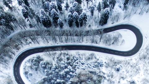 Eine sich schlängelnde Straße in verschneiter Waldlandschaft aus der Vogelperspektive.