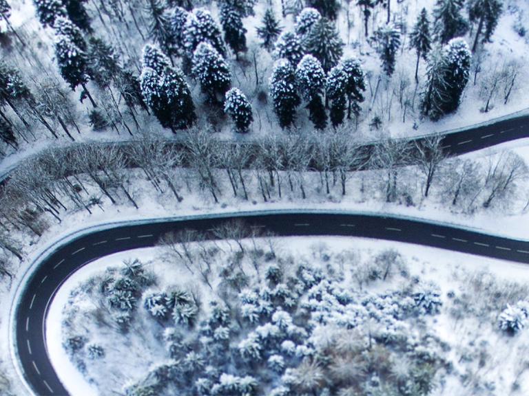 Eine sich schlängelnde Straße in verschneiter Waldlandschaft aus der Vogelperspektive.