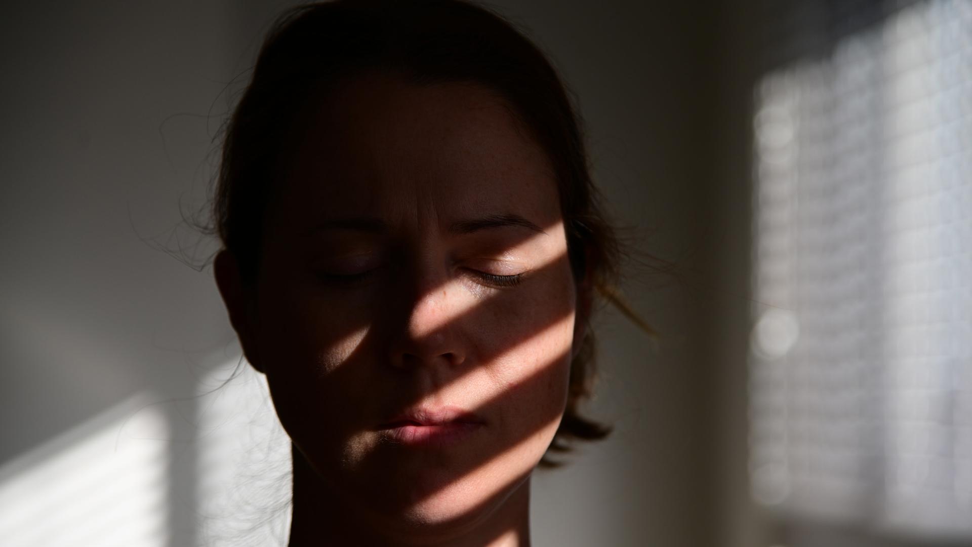 Porträt einer Frau mit geschlossenen Augen, auf deren Gesicht sich die Schatten einer Jalousie abzeichnen.