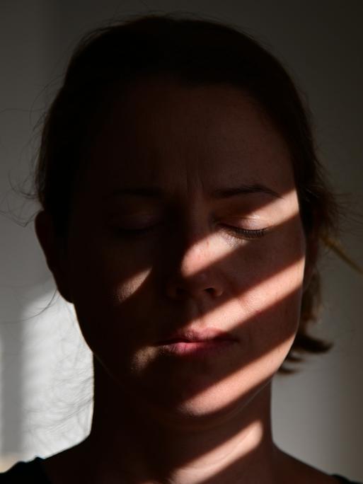Porträt einer Frau mit geschlossenen Augen, auf deren Gesicht sich die Schatten einer Jalousie abzeichnen.