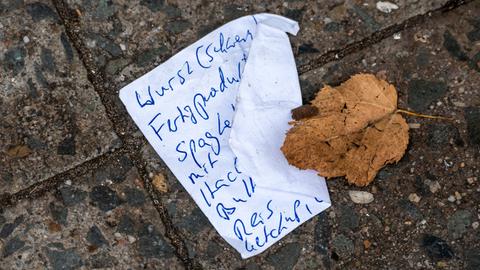 Ein Einkaufszettel liegt auf dem Boden, darauf ein verwelktes Blatt.