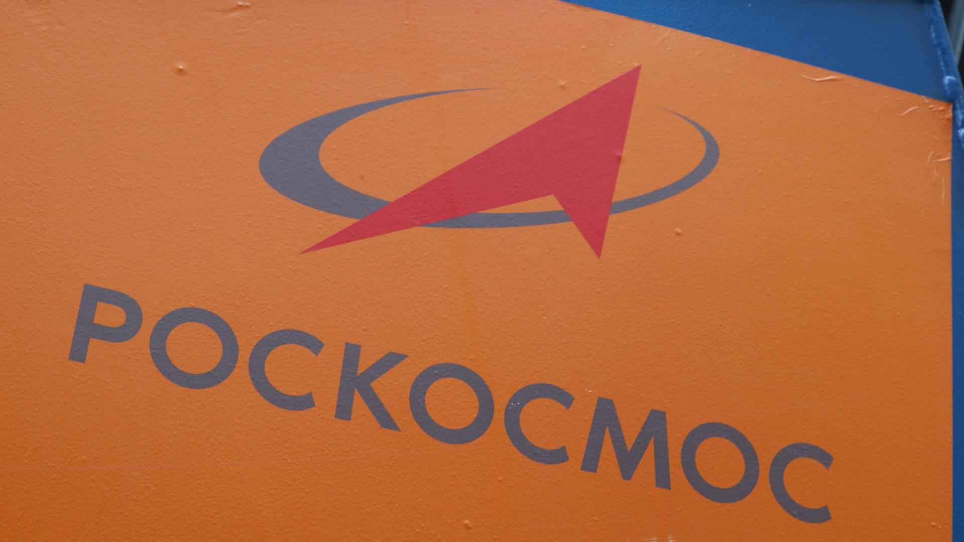 Zu sehen ist das Logo der russischen Raumfahrtbehörde Roskosmos auf orangefarbenem Hintergrund.