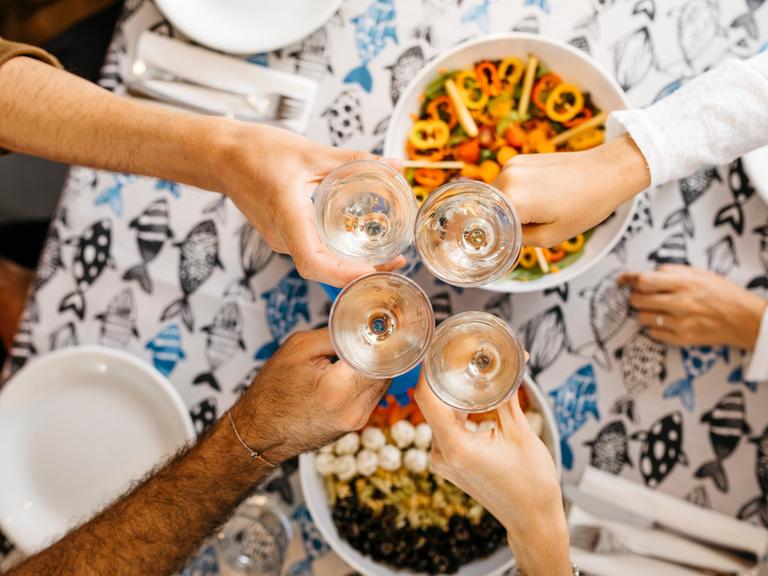 Ein Tisch einer Wohngemeimschaft beim gemeinsamen Essen, die Gläser prosten sich in der Mitte zu.