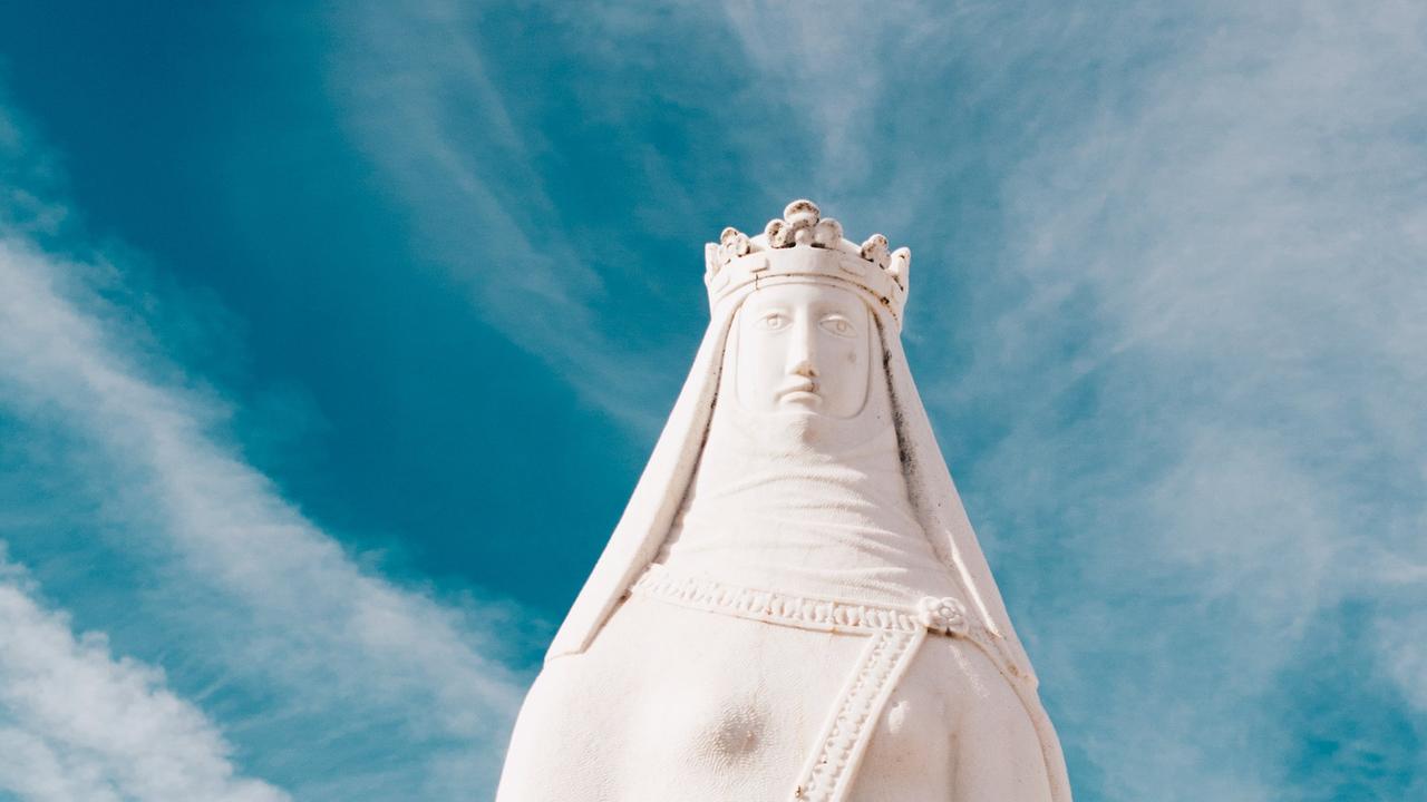 Eine schneeweiße Marienstatue mit Krone steht ernst vor einem blauen Himmel mit interessanten Schleierwolken.