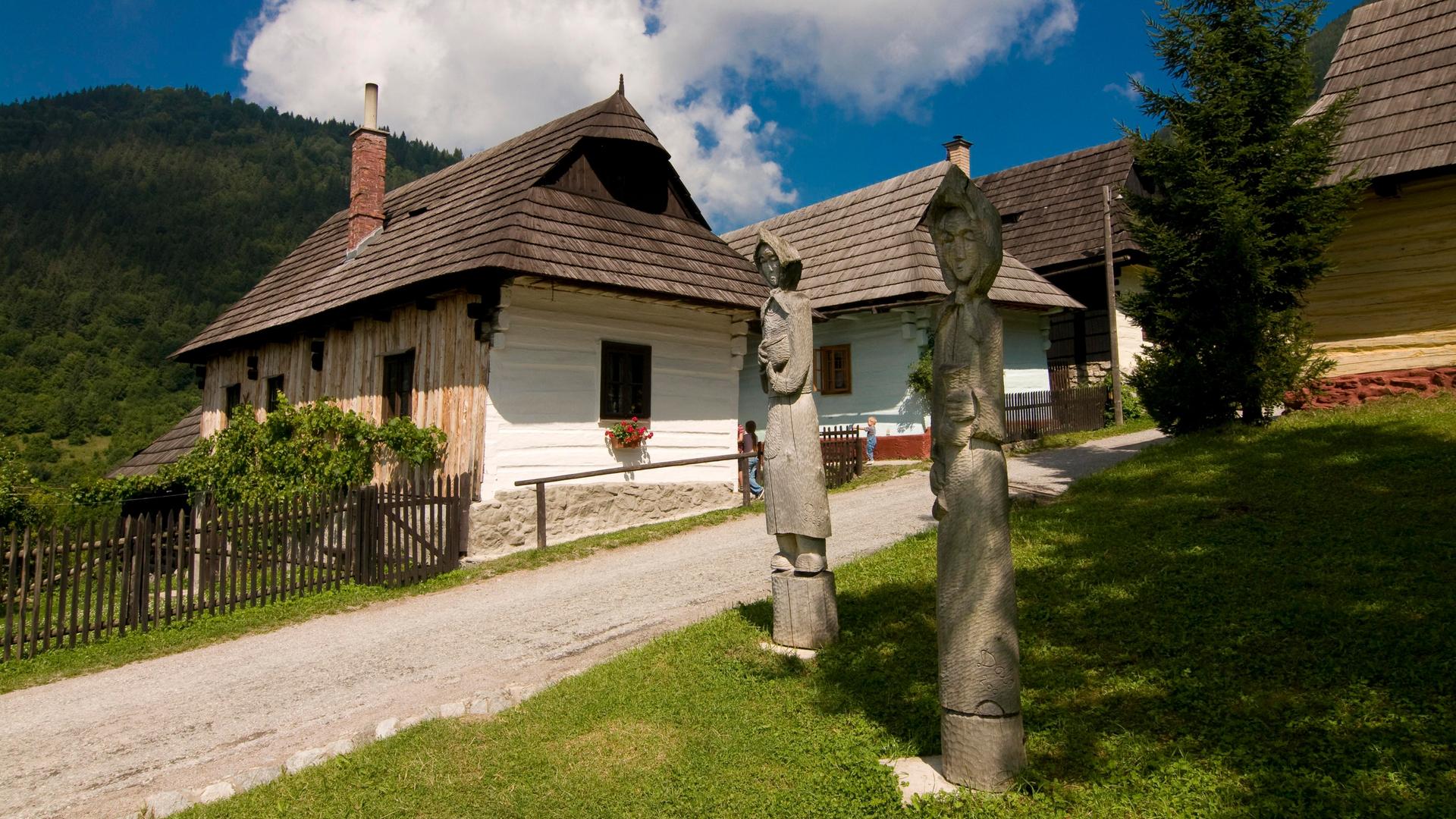 Holzfiguren stehen vor idyllischen Häusern im Bergdorf Vlkolínec in der Slowakei.
