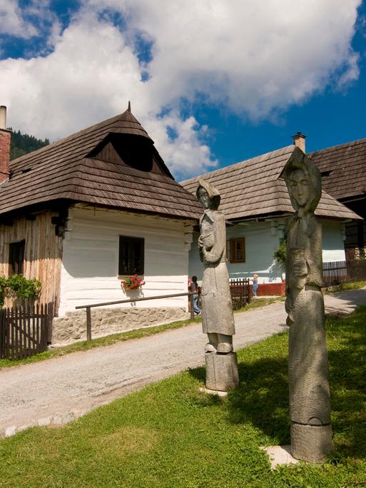 Holzfiguren stehen vor idyllischen Häusern im Bergdorf Vlkolínec in der Slowakei