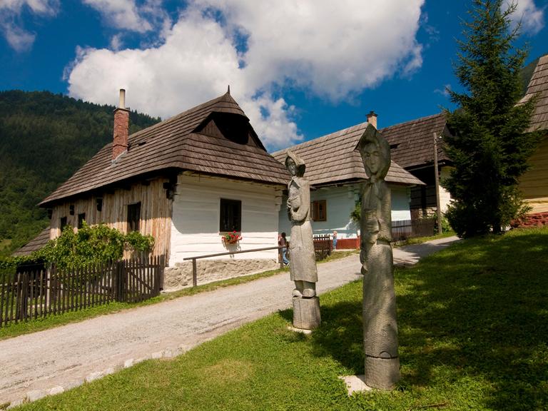 Holzfiguren stehen vor idyllischen Häusern im Bergdorf Vlkolínec in der Slowakei