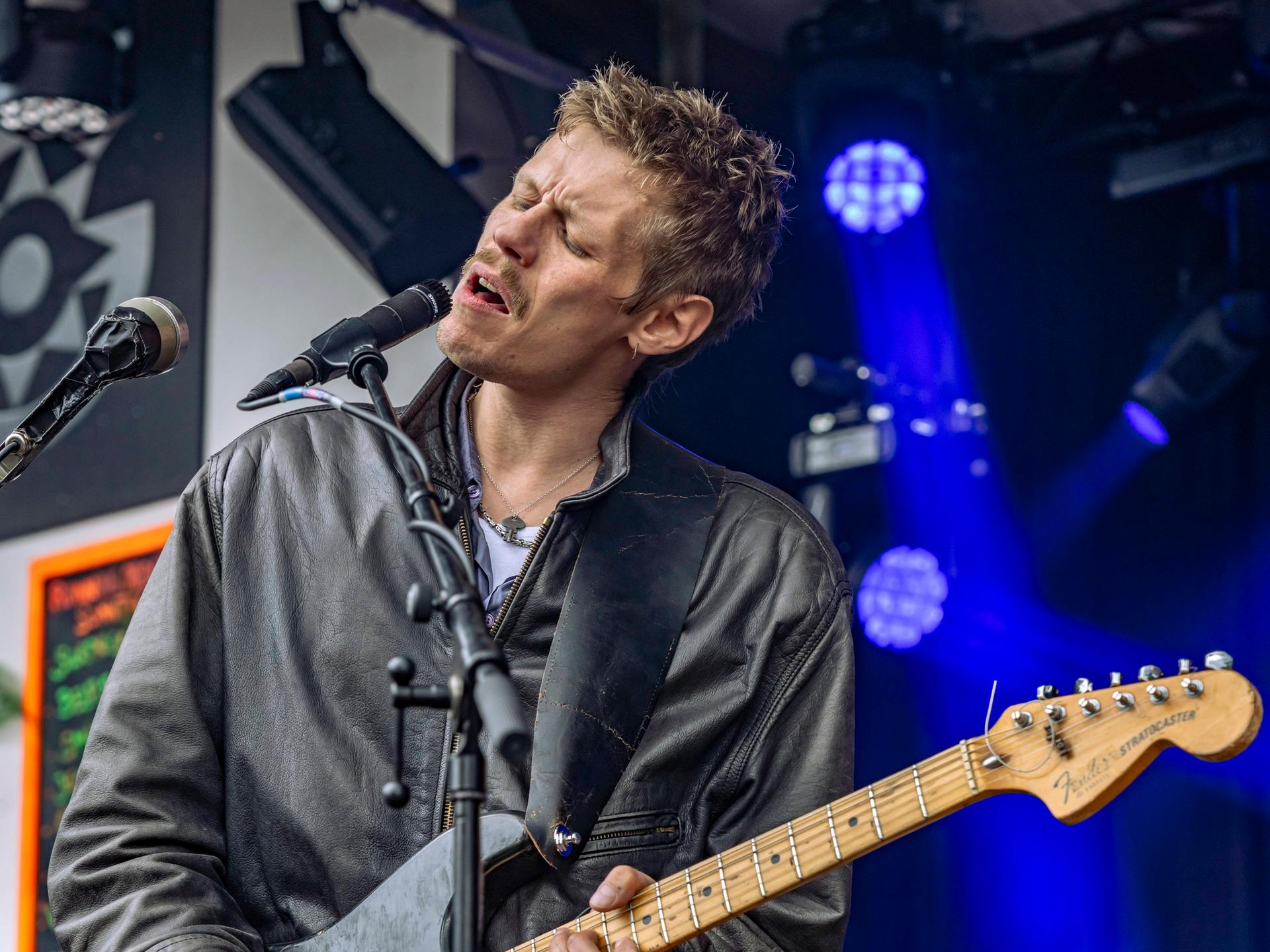 Wir sehen den Musiker Jesper Munk wie er gerade auf der Bühne steht, singt und Gitarre spielt. 