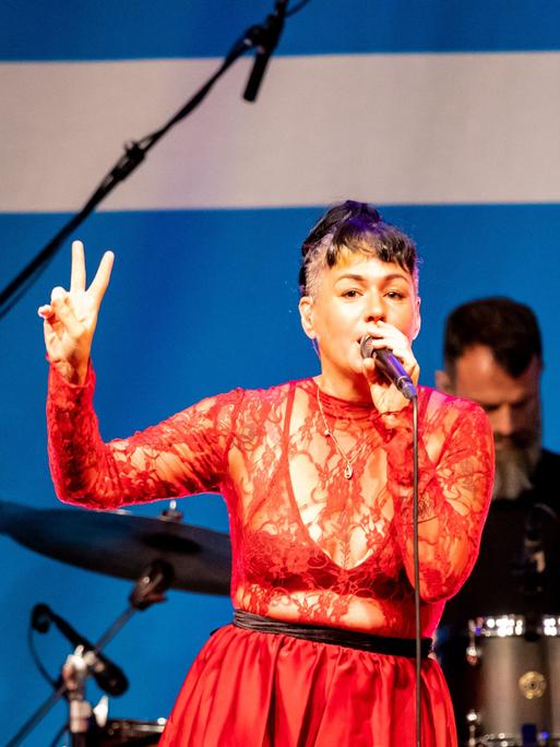 Sängerin Meghan Parnell steht in einem roten Spitzenoberteil auf der Bühne im Deutschlandfunk Kammermusiksaal und singt, während sie tanzt.