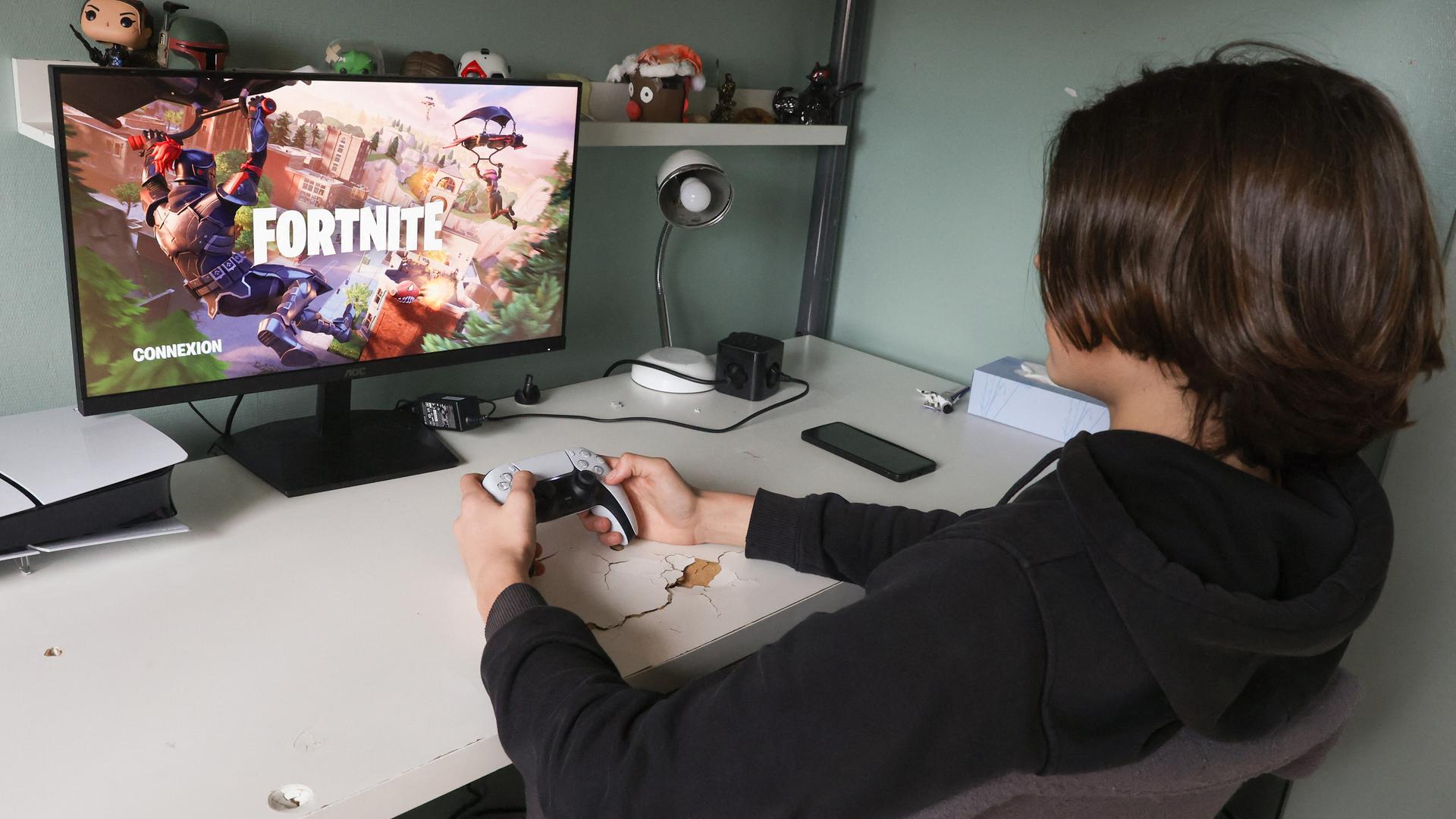Ein Teeanager sitzt mit Controller in der Hand vor einem Bildschirm und spielt das Computerspiel Fortnite. Ein Teeanager sitzt mit Controller in der Hand vor einem Bildschirm und spielt das Computerspiel Fortnite.