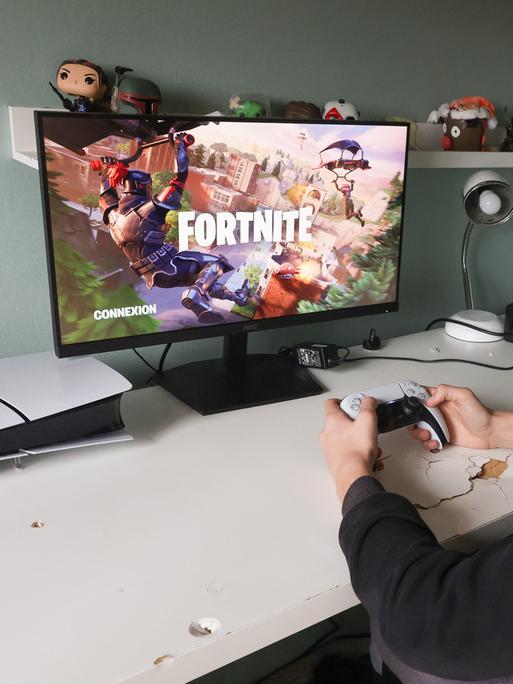 Ein Teeanager sitzt mit Controller in der Hand vor einem Bildschirm und spielt das Computerspiel Fortnite.