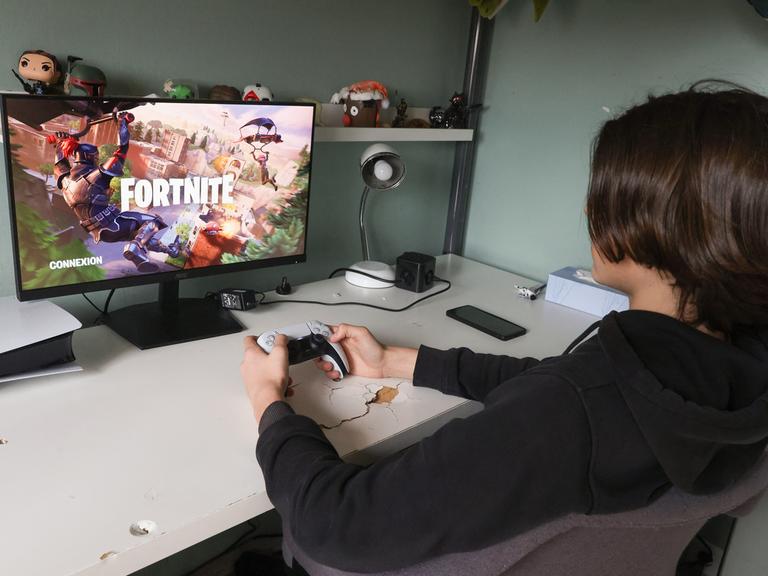 Ein Teeanager sitzt mit Controller in der Hand vor einem Bildschirm und spielt das Computerspiel Fortnite.