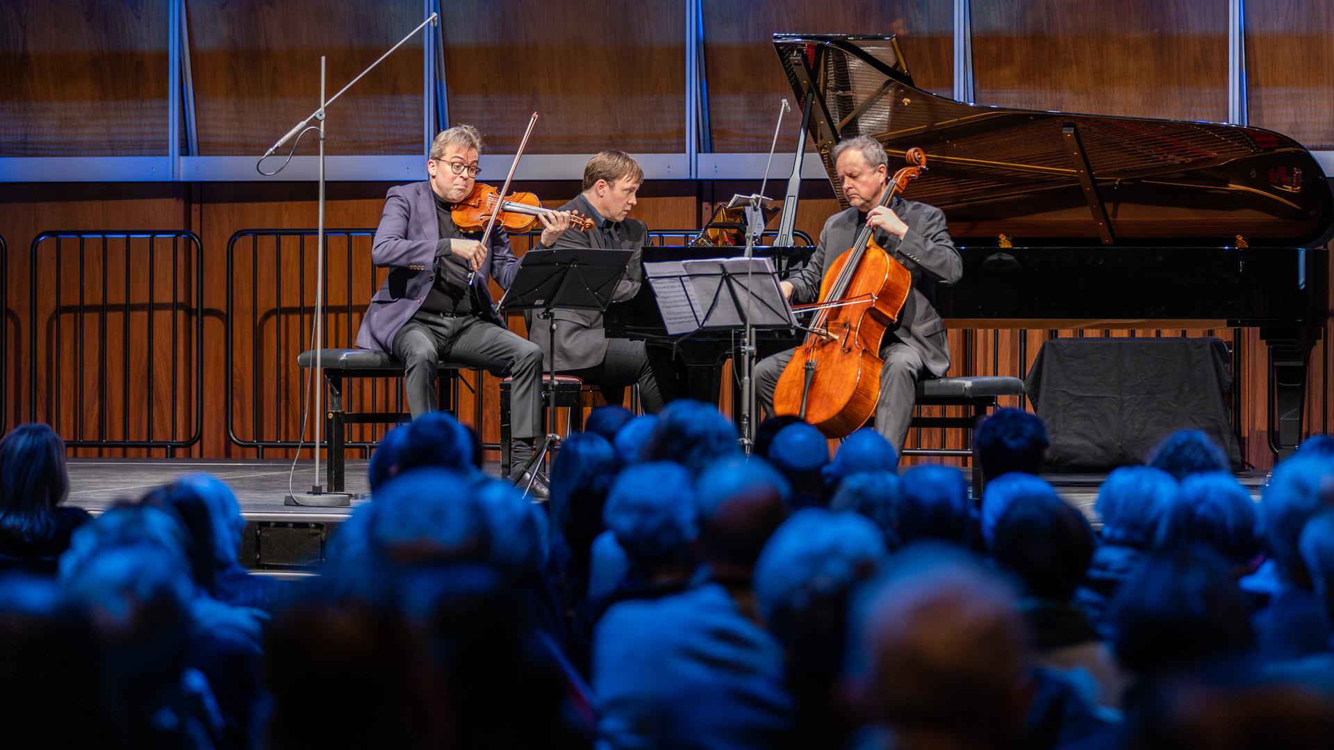 Ein Klaviertrio musiziert auf einer Bühne.