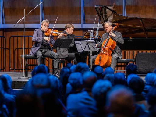 Ein Klaviertrio musiziert auf einer Bühne.