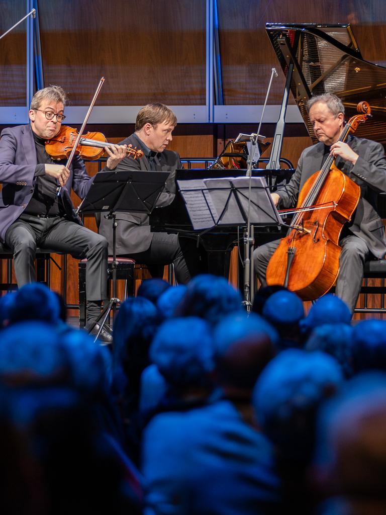 Ein Klaviertrio musiziert auf einer Bühne.