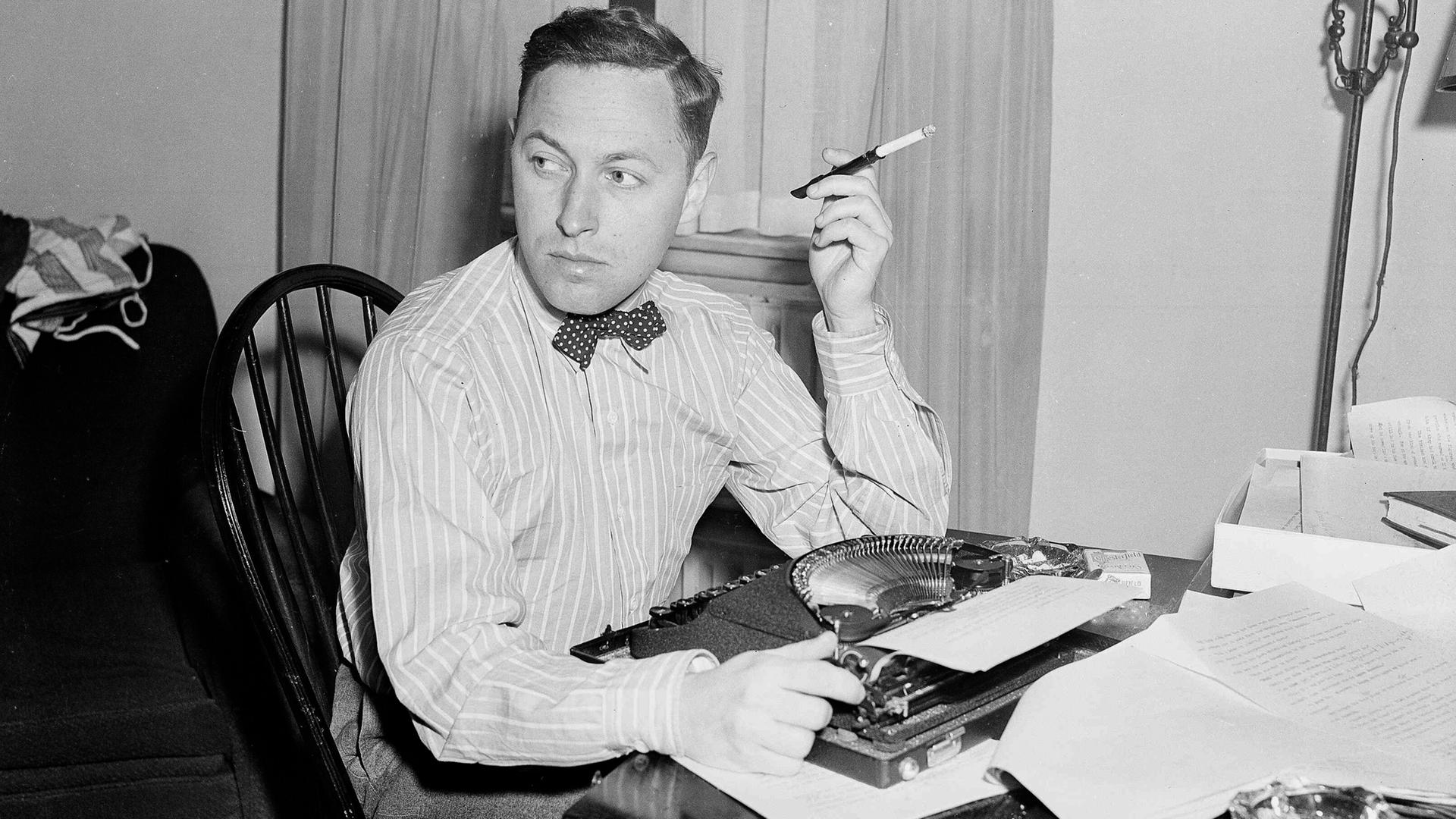 Der US-amerikanische Dramatiker Tennessee Williams an einem Tisch mit Schreibmaschine sitzend und Zigarette rauchend