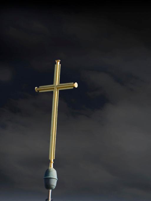 Das Kreuz einer Kirche vor dunklen Wolken.
