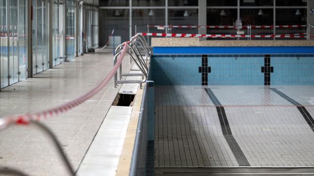 Ein leeres Schwimm-Becken ohne Wasser ist mit rot-weißem Band abgesperrt. 