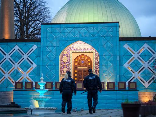 Zwei Polizisten stehen im Abendlicht vor der beleuchteten Imam-Ali-Moschee des Islamischen Zentrums Hamburg. Zwei Polizisten stehen im Abendlicht vor der beleuchteten Imam-Ali-Moschee des Islamischen Zentrums Hamburg.
