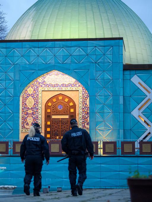 Zwei Polizisten stehen im Abendlicht vor der beleuchteten Imam-Ali-Moschee des Islamischen Zentrums Hamburg. Zwei Polizisten stehen im Abendlicht vor der beleuchteten Imam-Ali-Moschee des Islamischen Zentrums Hamburg.
