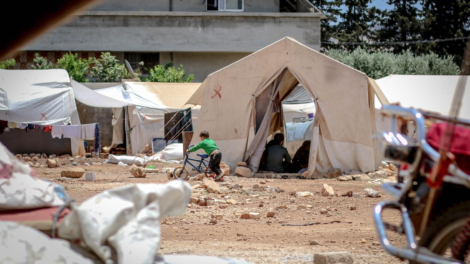 Ein Kind spielt vor einem Zelt im Flüchtlingslager.