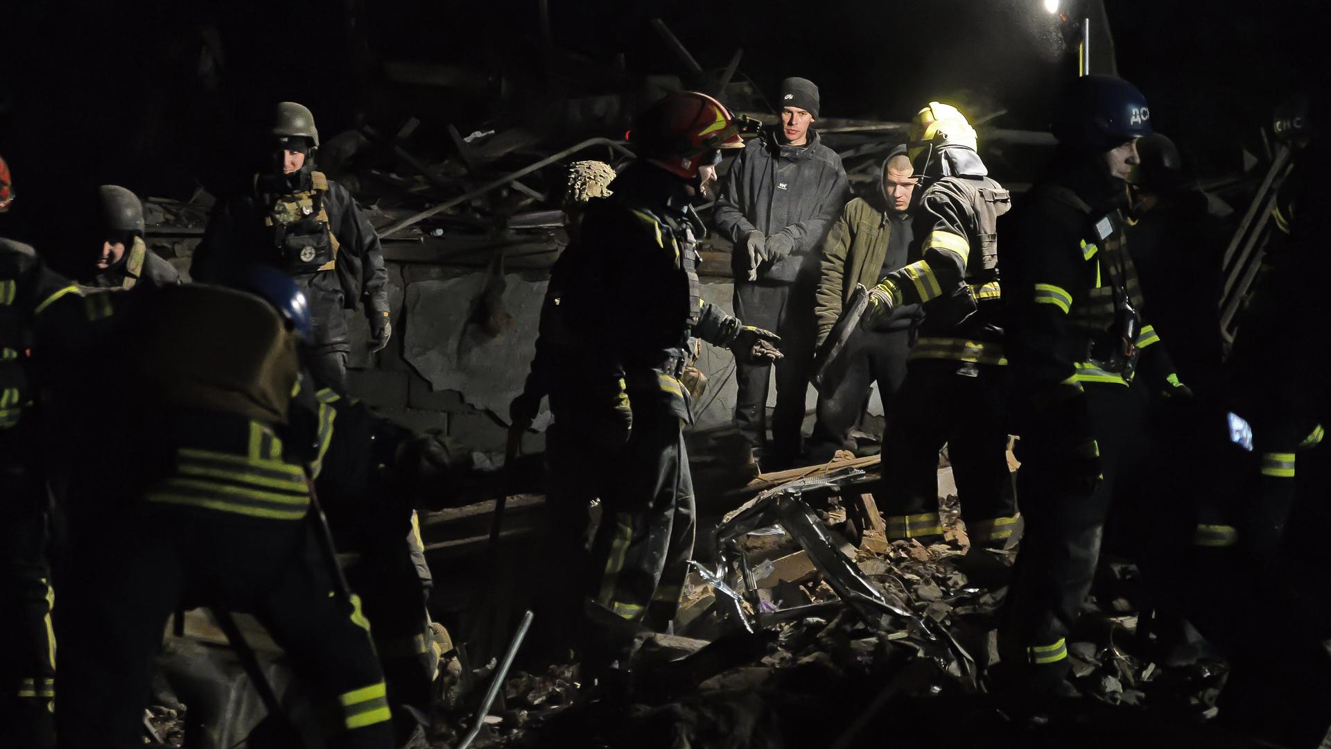 Mehrere Rettungskräfte stehen im Dunkeln neben den Trümmern eines Autos.