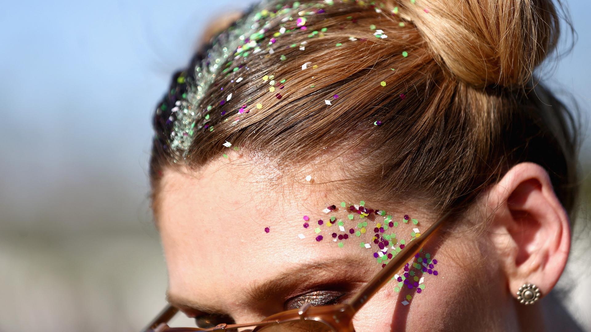 Nahaufnahme einer Frau mit blonder Hockstecksfrisur, die ihr Haar und Gesicht für ein Festival mit Glitzer dekoriert hat.