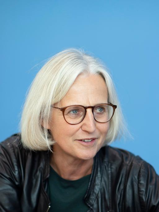 Die Autorin Christiane Hoffmann im Portrait von der Seite. Sie trägt eine Brille, hat blonde kurze Haare und trägt dunkle Kleidung. 