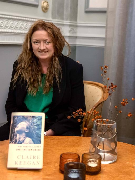 Die irische Autorin Claire Keegan sitzt an einem runden Tisch, vor ihr ist ihr Buch aufgestellt. 
