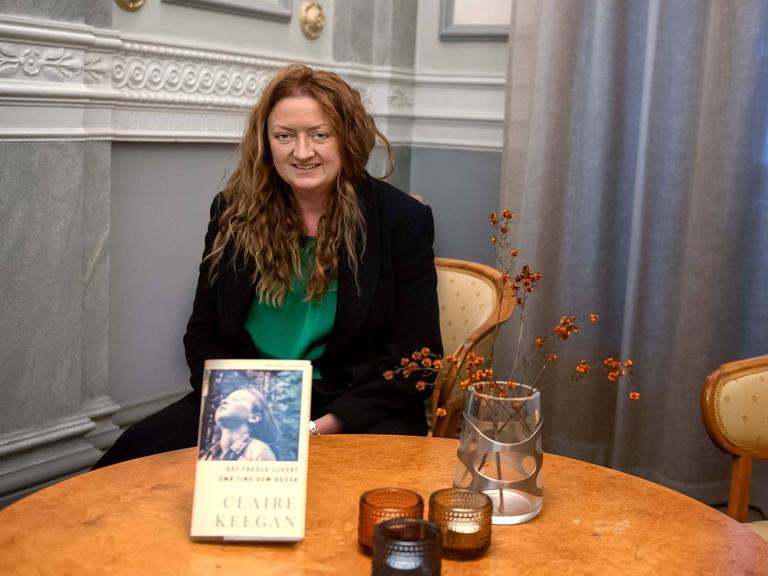 Die irische Autorin Claire Keegan sitzt an einem runden Tisch, vor ihr ist ihr Buch aufgestellt. 