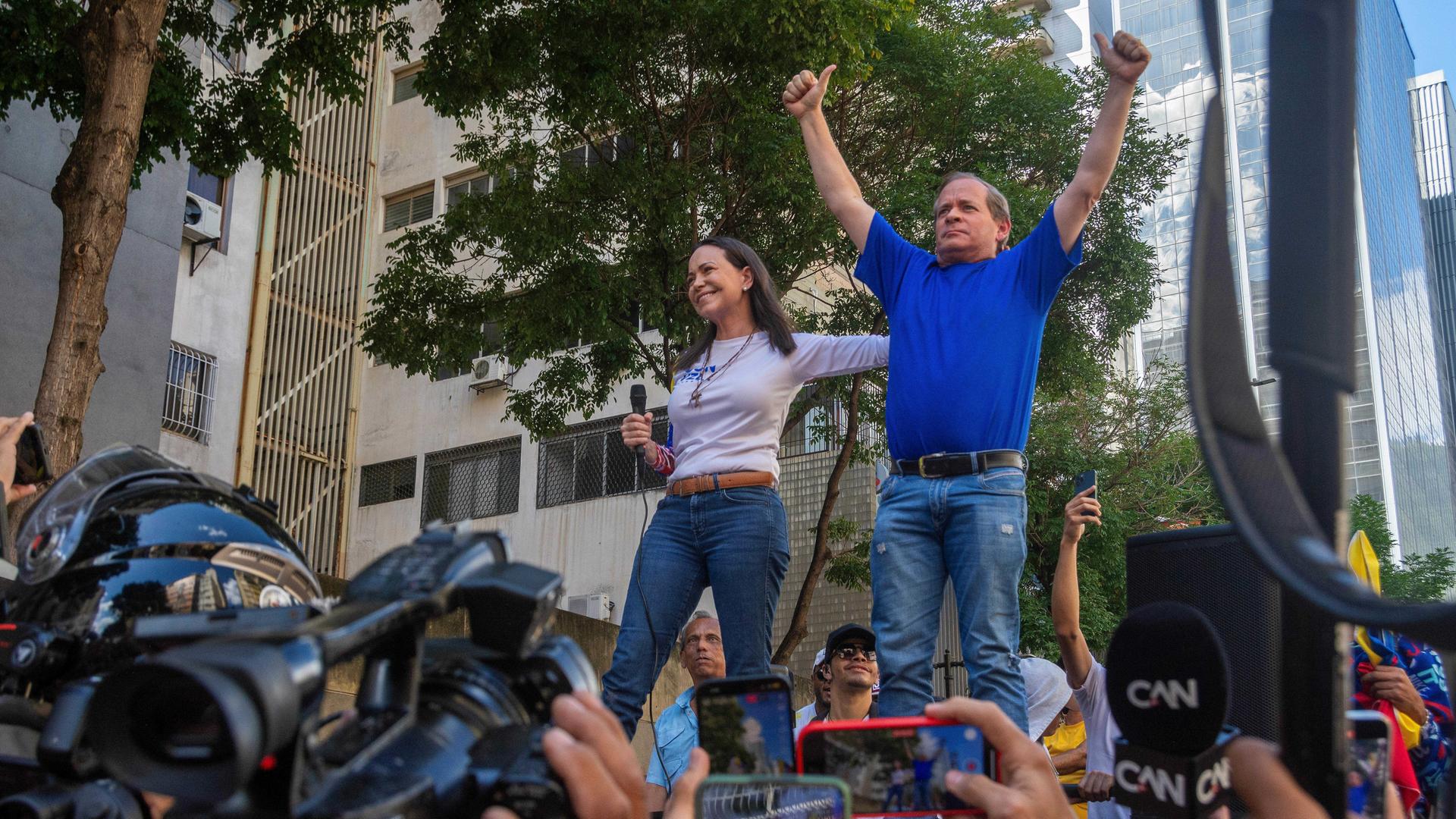 In einer Menschenmenge stehen María Machado und Juan Pablo Guanipa nebeneinander. Er streckt beide Daumen nach oben.