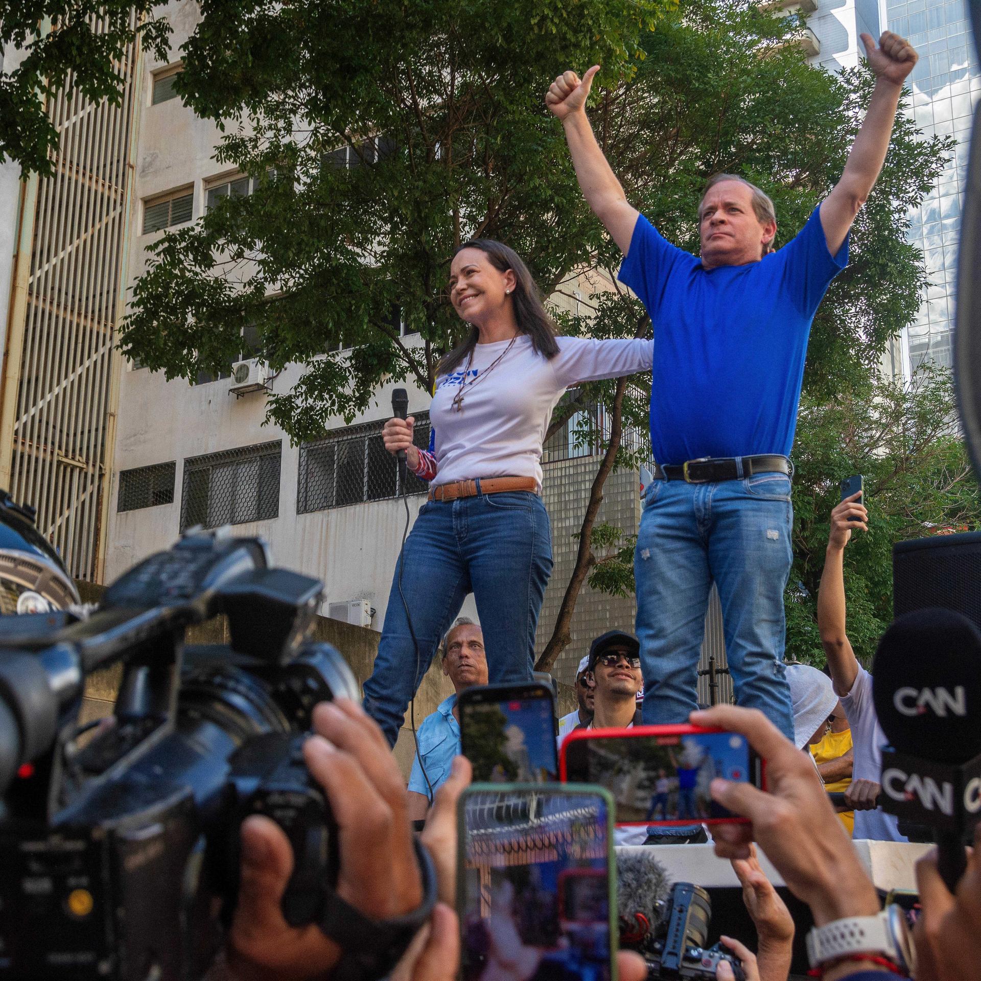 In einer Menschenmenge stehen María Machado und Juan Pablo Guanipa nebeneinander. Er streckt beide Daumen nach oben.