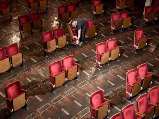 Ein Mitarbeiter trägt Stühle aus den Sitzreihen des Zuschauerraums des Berliner Ensembles. Wegen der Kontakteinschränkungen während der Coronapandemie werden einzelne Sitze für zukünftige Aufführungen ausgebaut.