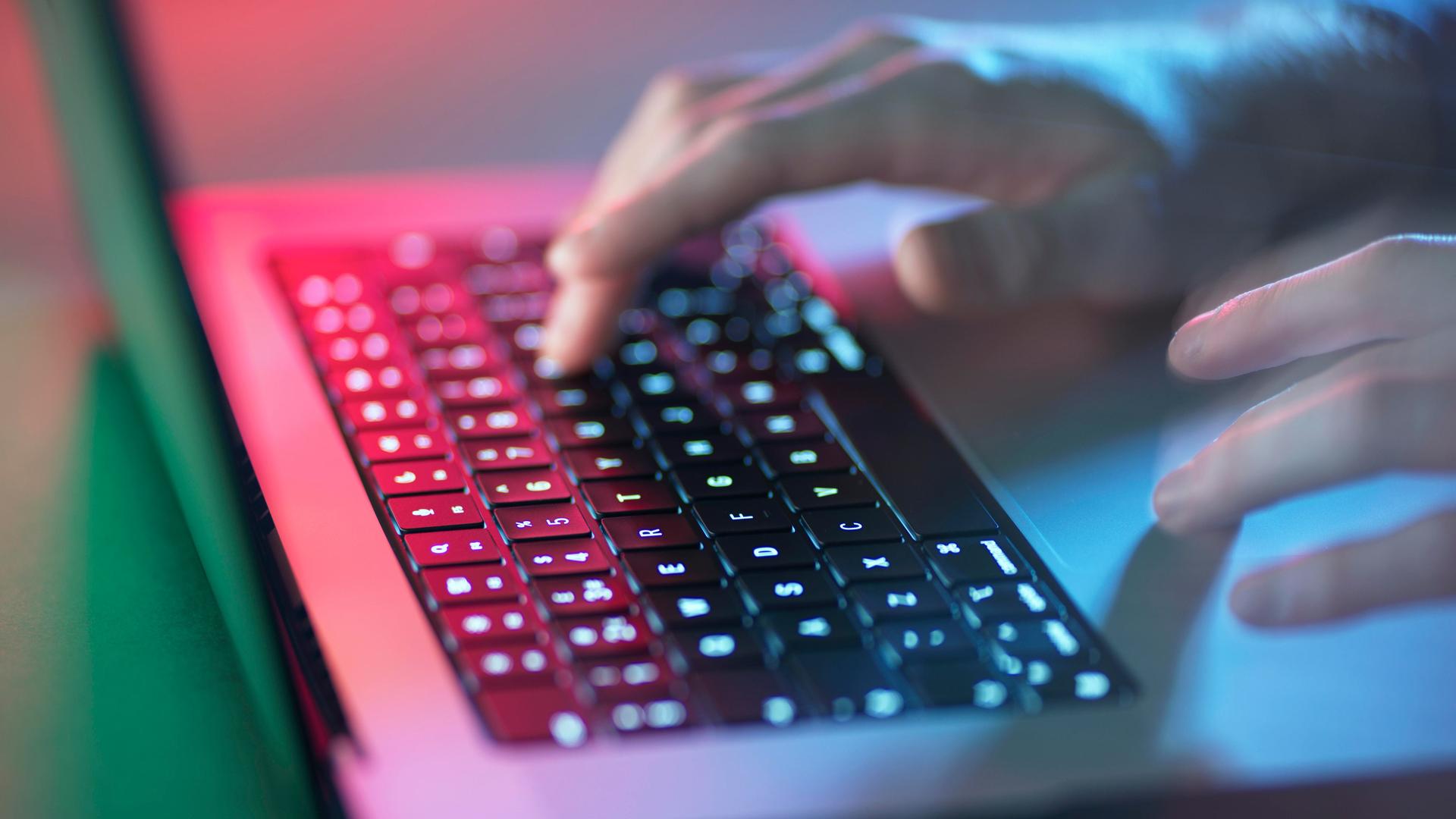 Hände auf der Tastatur eines Laptops im Zwielicht.