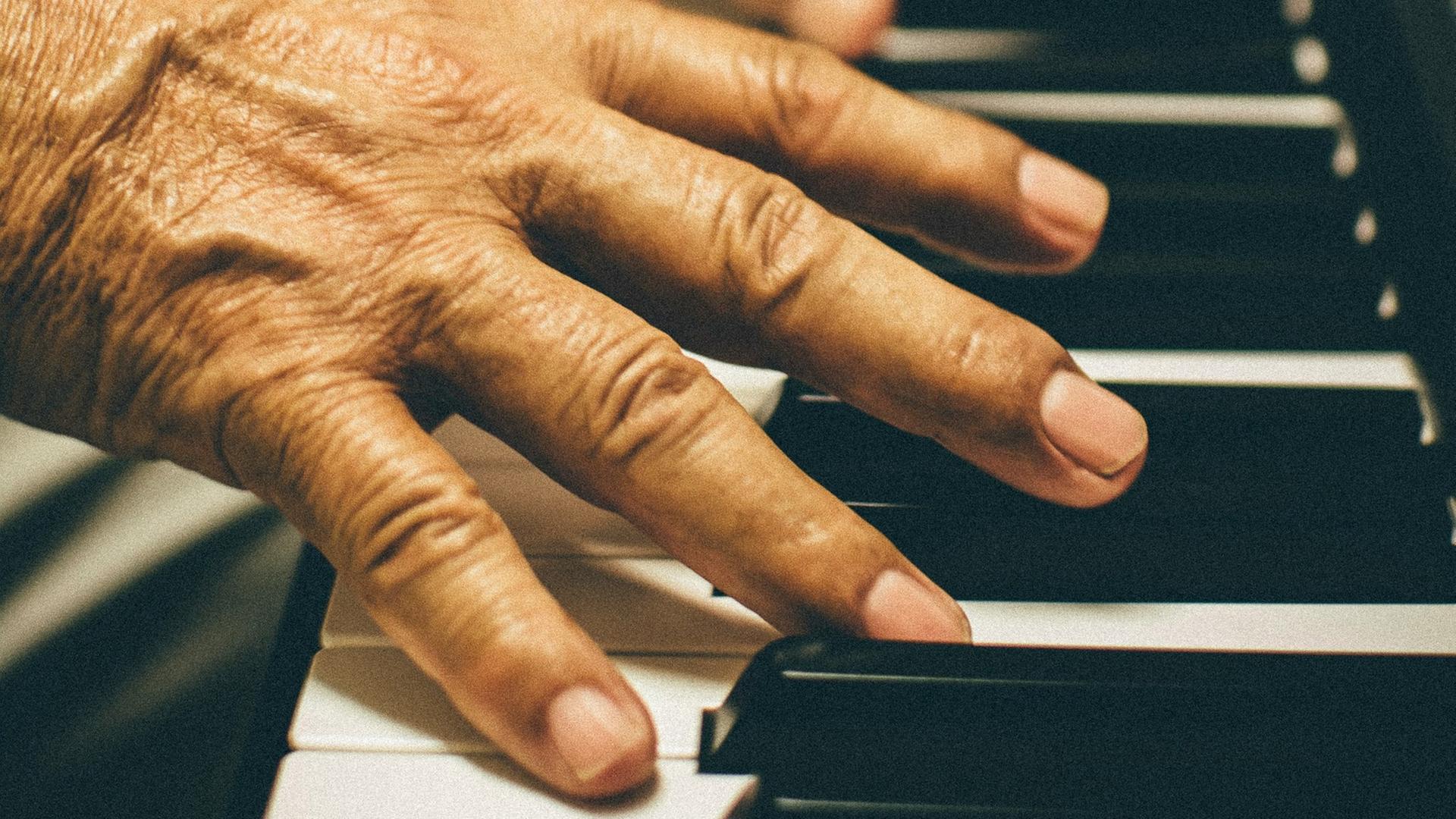 Hände eines älteren Mannes liegen auf den Tasten einer Klaviatur.