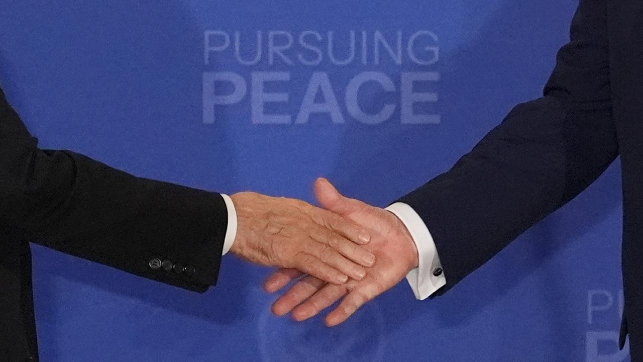 Zwei Hände nähern sich zum Handshake vor blauem Hintergrund; darauf steht "Pursuing Peace". Zwei Hände nähern sich zum Handshake vor blauem Hintergrund; darauf steht "Pursuing Peace".