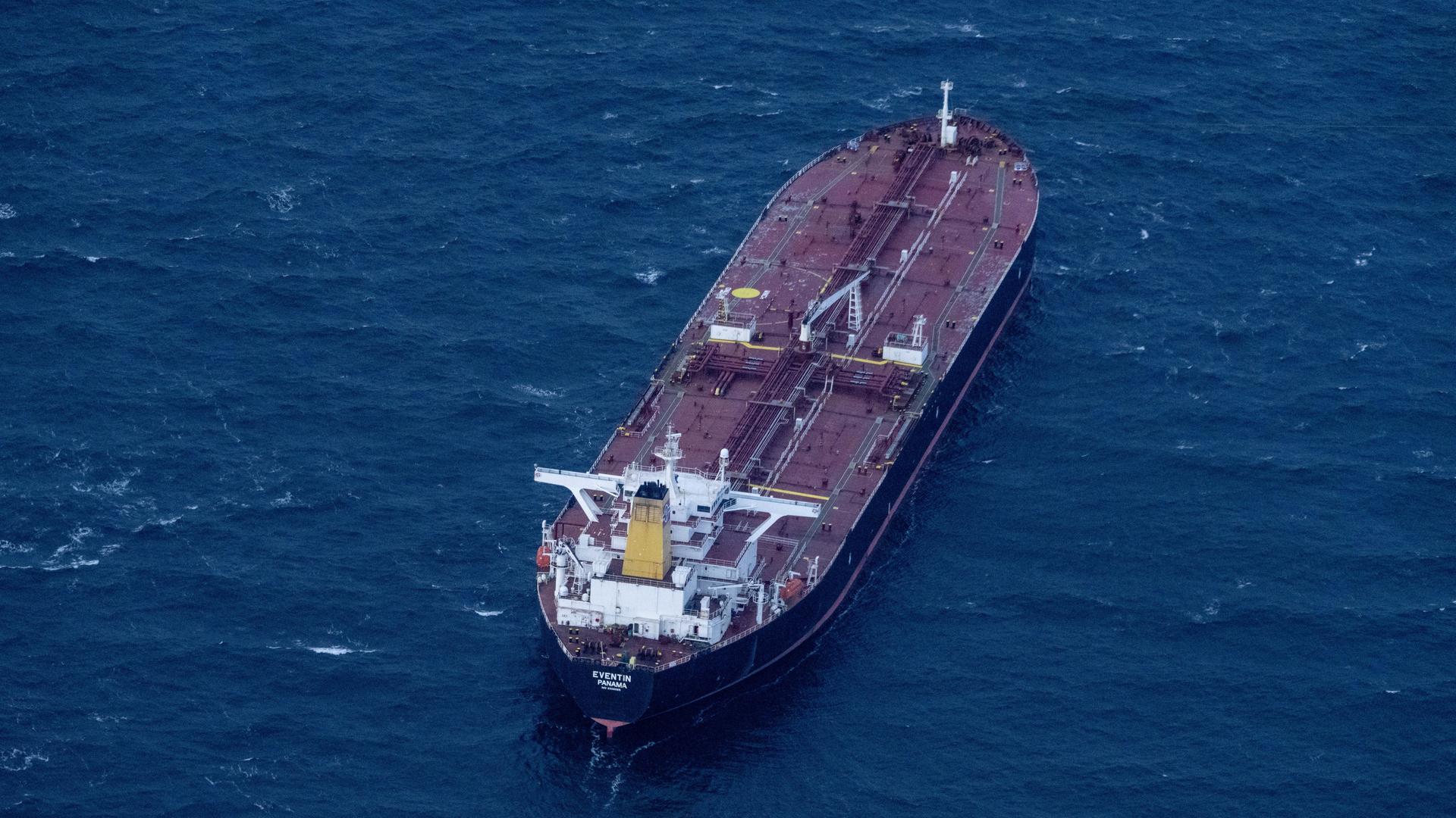 Blick aus großer Höhe auf den rostbraunen Tanker im dunkelblauen Meer. 