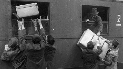 Historische schwarz-weiß Aufnahme: Ankommende "Gastarbeiter" entladen Koffer auf einem Bahnsteig im Hauptbahnhof München ca. 1970.