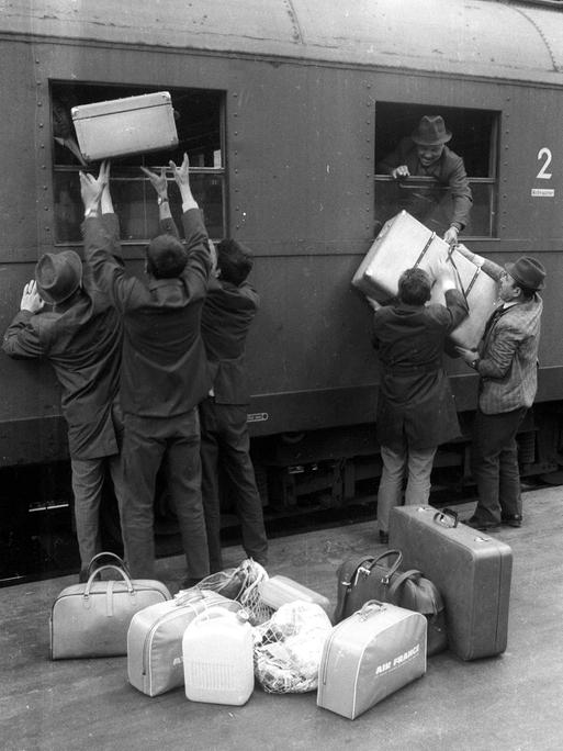 Historische schwarz-weiß Aufnahme: Ankommende "Gastarbeiter" entladen Koffer auf einem Bahnsteig im Hauptbahnhof München ca. 1970.