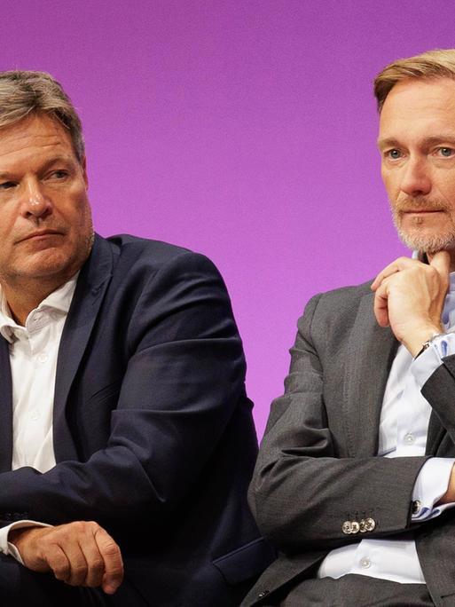 Bundeswirtschaftsminister Robert Habeck und Bundesfinanzminister Christian Lindner sitzen auf einem Podium und gucken beide nachdenklich.