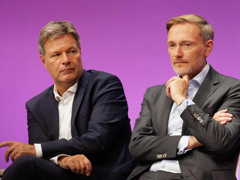 Bundeswirtschaftsminister Robert Habeck und Bundesfinanzminister Christian Lindner sitzen auf einem Podium und gucken beide nachdenklich.