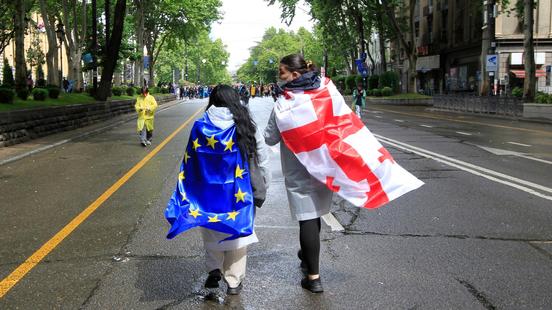 Zwei Demonstranten haben sich die georgische und die EU-Flagge umgebunden und laufen damit eine Straße in Tiflis entlang.