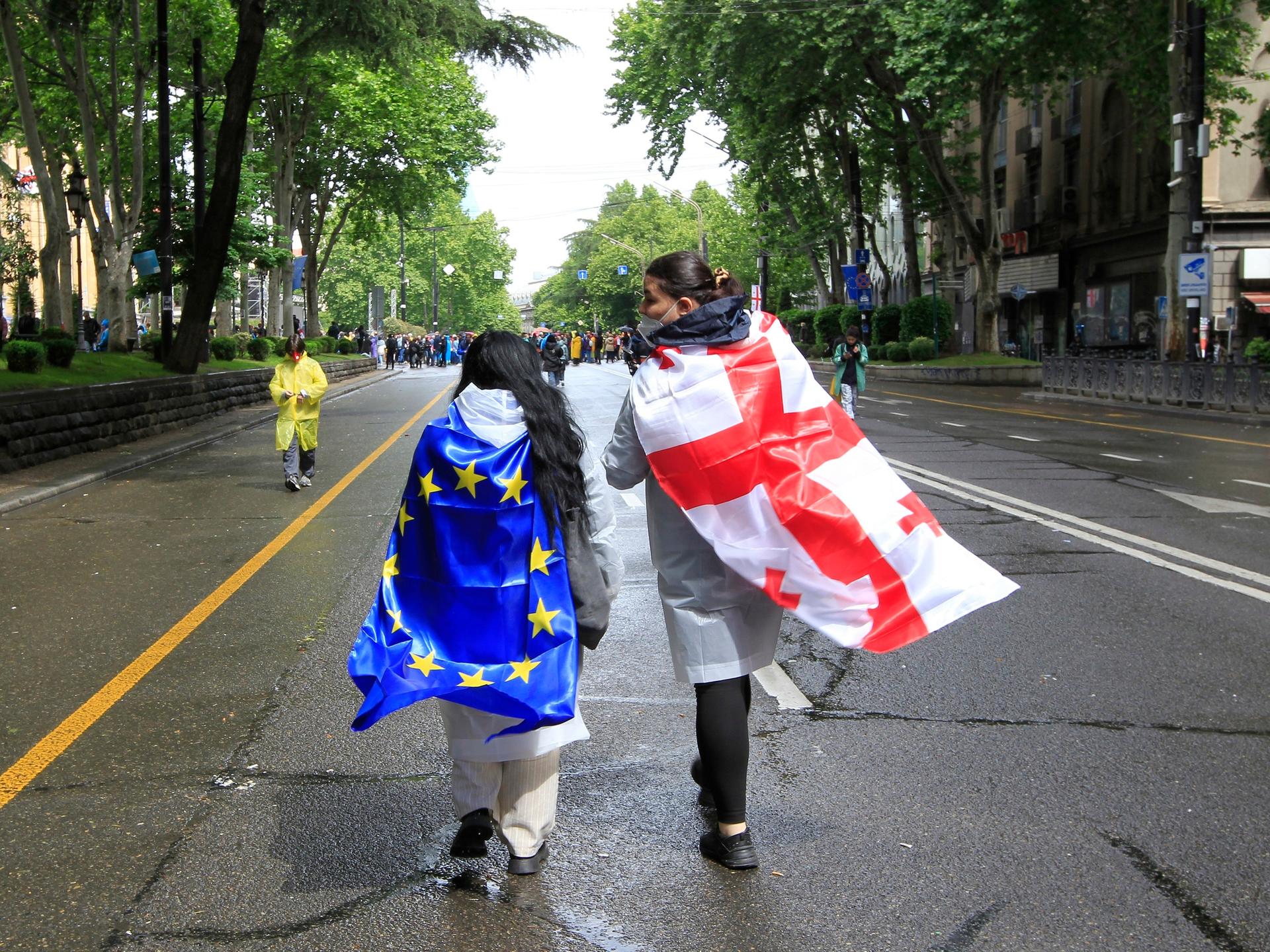 Zwei Demonstranten haben sich die georgische und die EU-Flagge umgebunden und laufen damit eine Straße in Tiflis entlang.