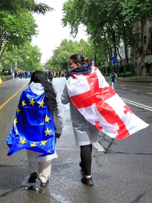 Zwei Demonstranten haben sich die georgische und die EU-Flagge umgebunden und laufen damit eine Straße in Tiflis entlang.