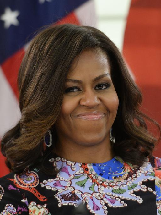 Michelle Obama steht lächeln vor einer amerikanischen Flagge.