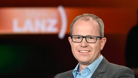 Der Immunologe Carsten Watzl sitzt in einem Fernsehstudio und lächelt in die Kamera.