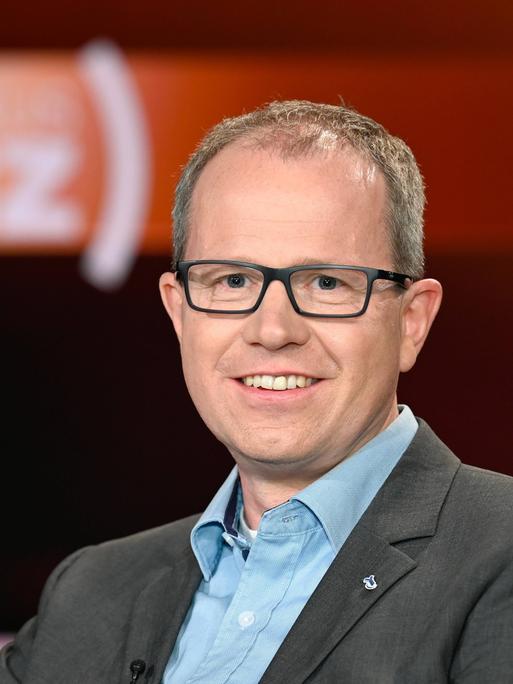 Der Immunologe Carsten Watzl sitzt in einem Fernsehstudio und lächelt in die Kamera.